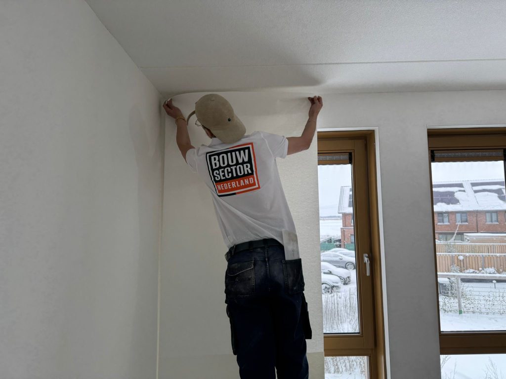 Behanger van Bouwsector Nederland zet een baan vlies strak tegen het plafond in een nieuwbouwwoning
